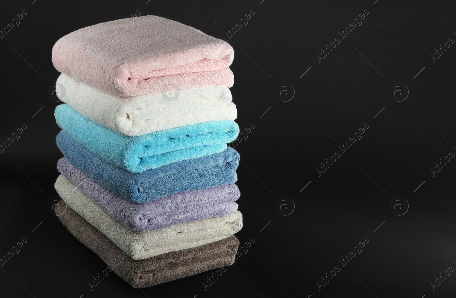 Photo of Different fresh soft terry towels on dark background. Space for text