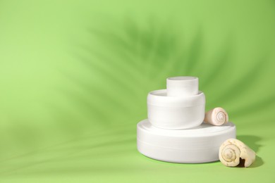 Photo of Jars of cream, lip balm and seashells on light green background, space for text