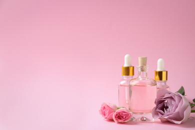 Photo of Bottles of essential oil and flowers on pink background. Space for text