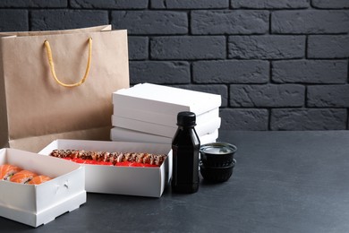 Food delivery. Boxes with delicious sushi rolls, paper package and soy sauce on black table, space for text