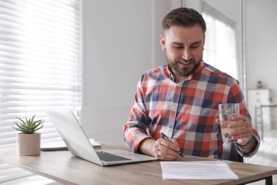 Young man with glass of water working at table in office