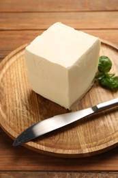 Photo of Block of tasty butter, knife and basil on wooden table