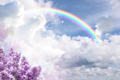 Fantasy world. Beautiful rainbow in sky with fluffy clouds over lilac flowers