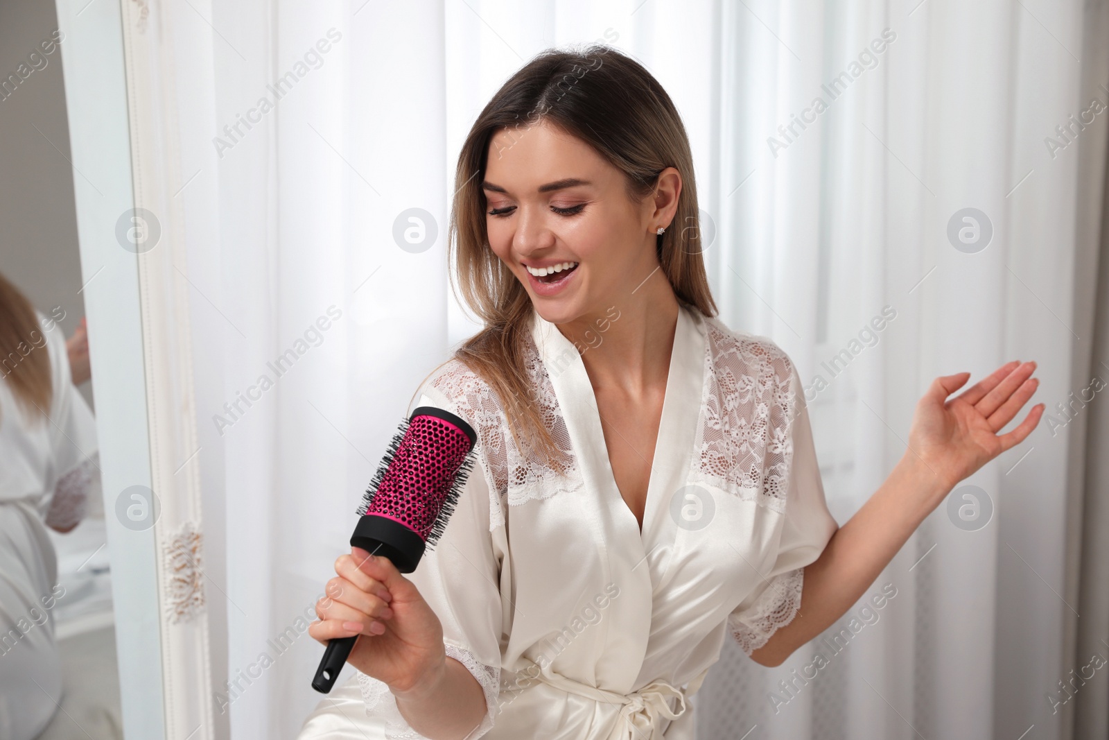 Photo of Beautiful woman with hairbrush singing in bedroom