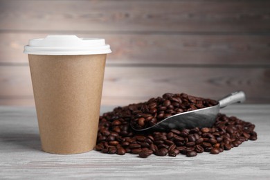 Photo of Coffee to go. Paper cup, roasted beans and scoop on light wooden table