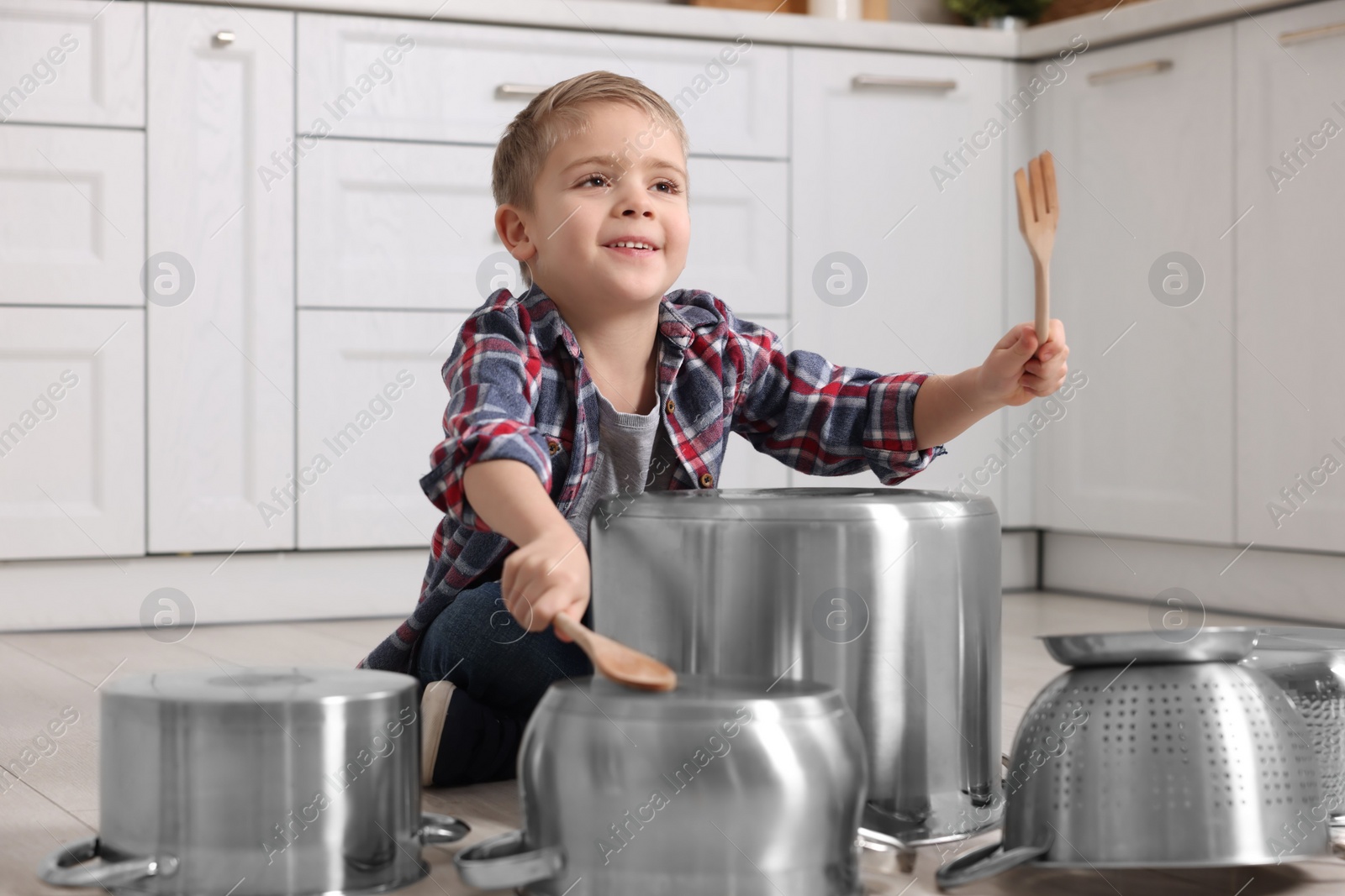 Photo of Little boy pretending to play drums on pots in kitchen