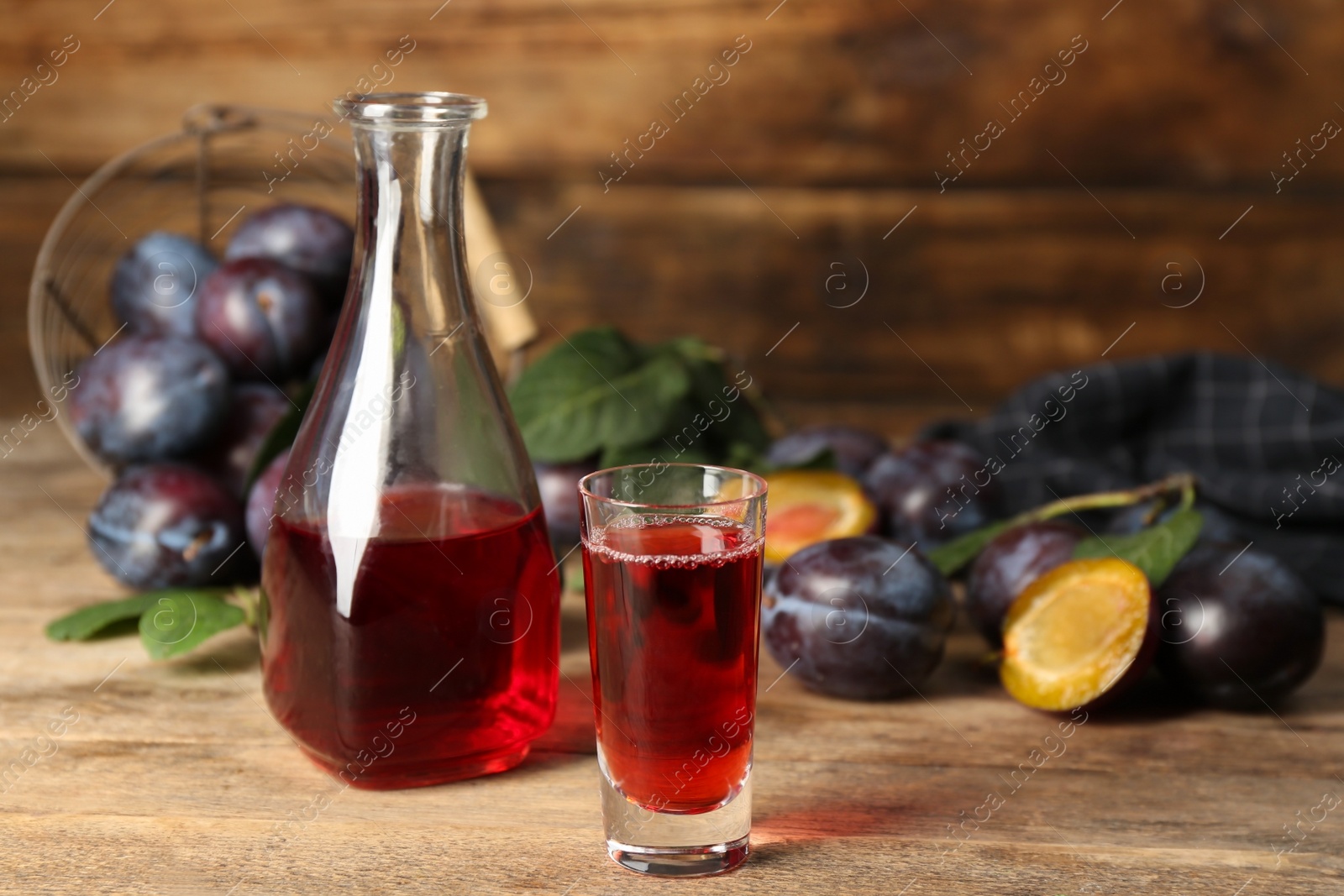 Photo of Delicious plum liquor and ripe fruits on wooden table. Homemade strong alcoholic beverage