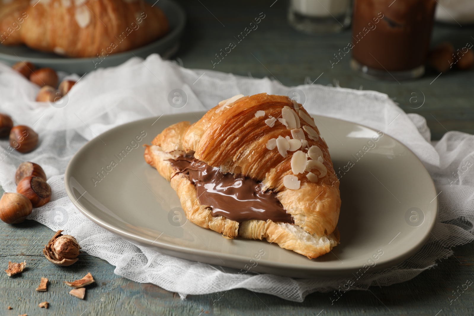 Photo of Delicious croissant with chocolate and nuts on light blue wooden table