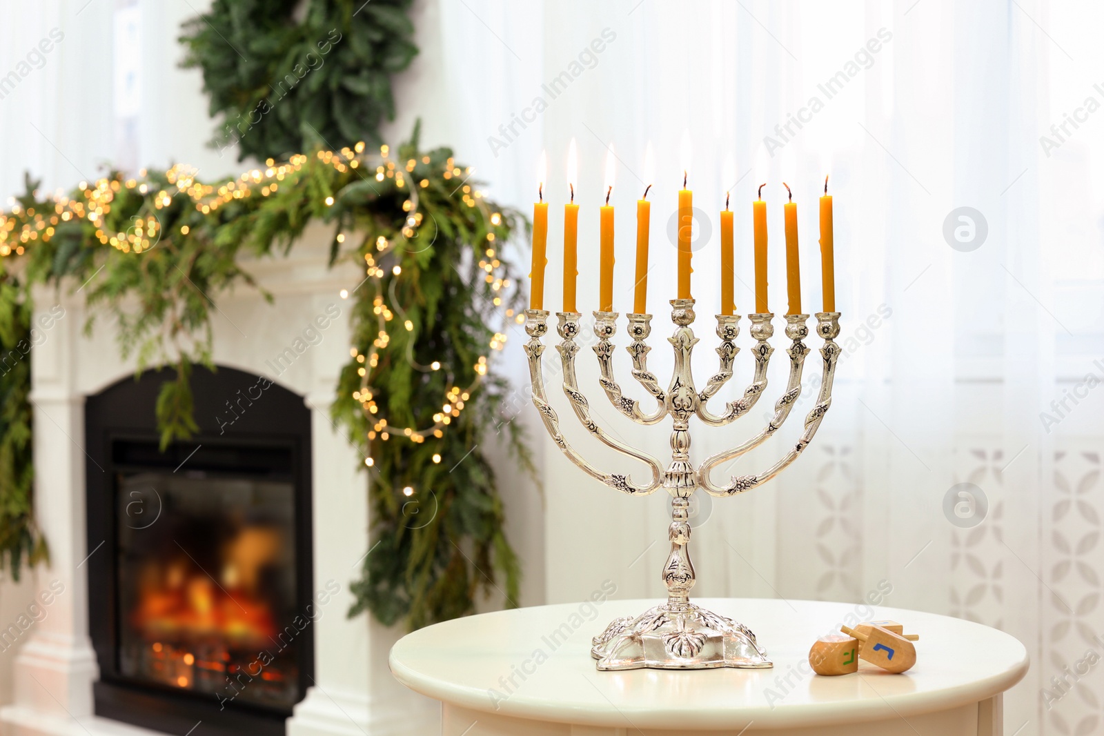 Photo of Silver menorah near dreidels with symbols He, Pe, Nun, Gimel on white table in room, space for text