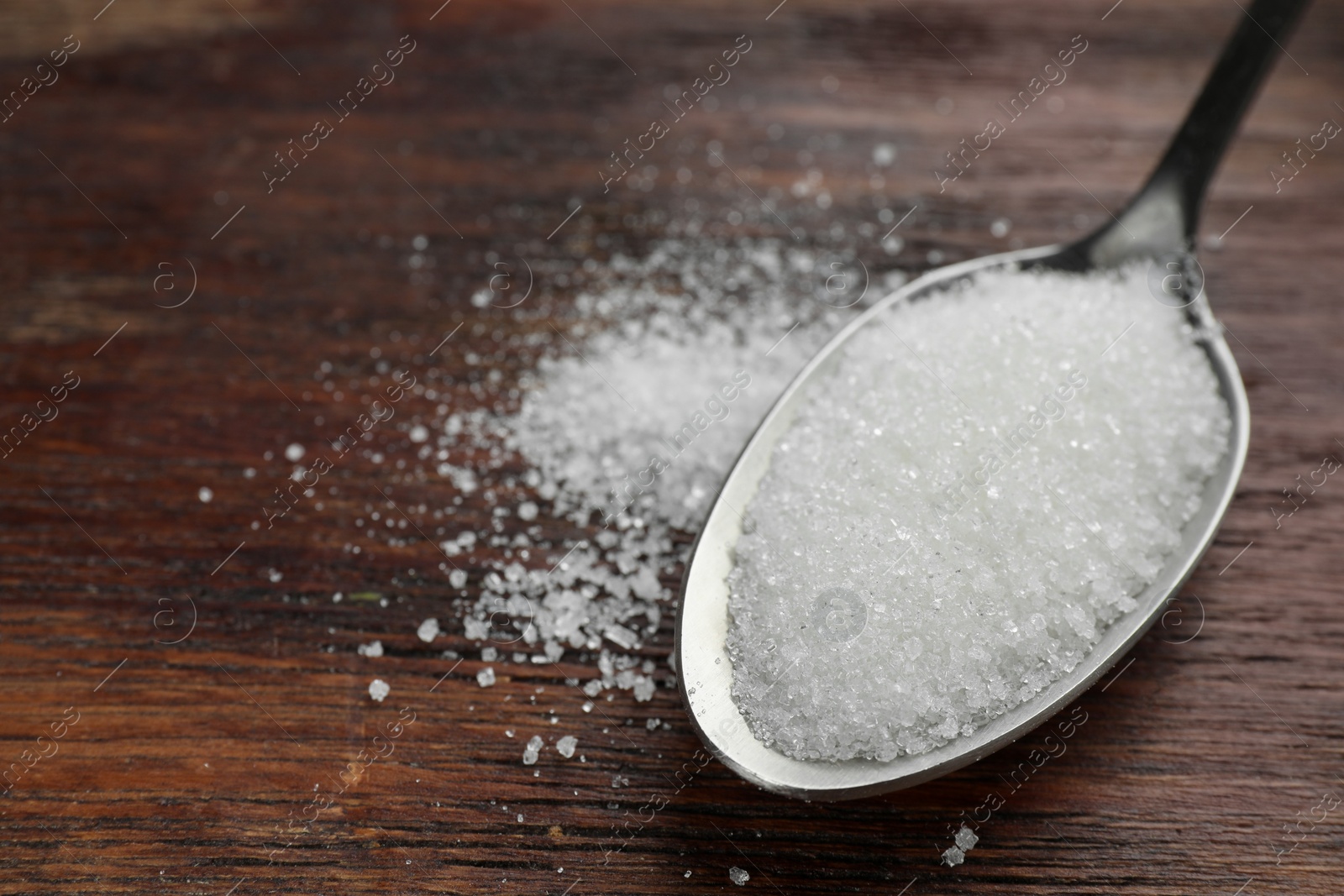 Photo of Spoon with granulated sugar on wooden table, closeup. Space for text