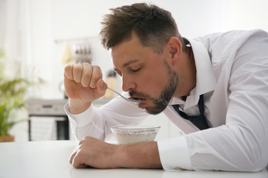 Sleepy man eating breakfast at home in morning