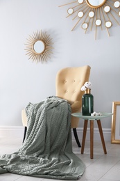 Photo of Soft knitted blanket on armchair in room. Home interior