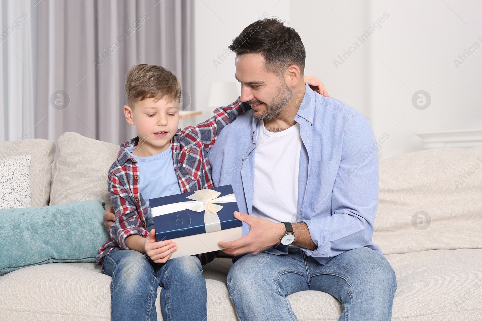 Photo of Cute little boy presenting his father with gift on sofa at home