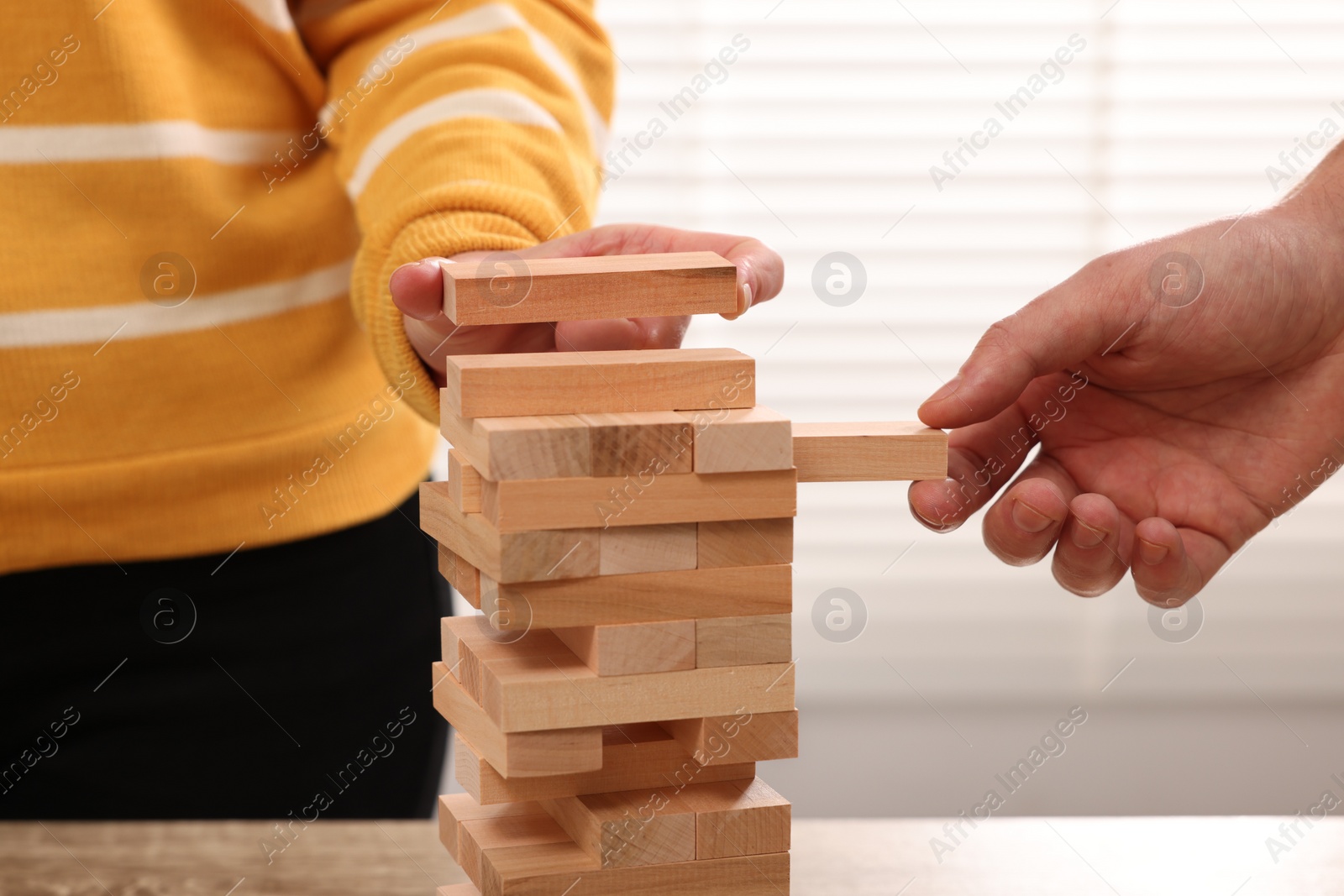Photo of People playing Jenga tower at table indoors, closeup