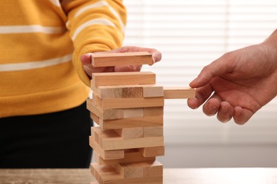 People playing Jenga tower at table indoors, closeup