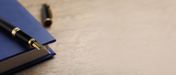 Image of Beautiful fountain pen and blue notebook on wooden table, closeup view with space for text. Banner design