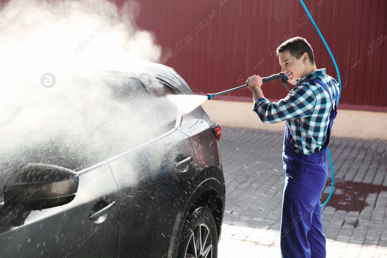 Photo of Worker cleaning automobile with high pressure water jet at car wash