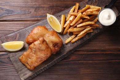 Photo of Tasty fish, chips, lemon and sauce on wooden table, top view