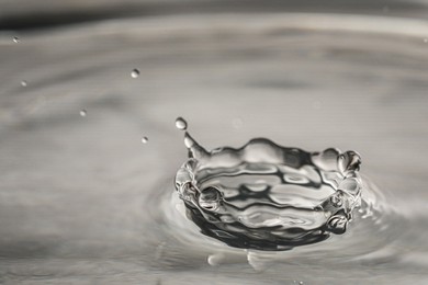 Photo of Splash of clear water with drops on grey background, closeup