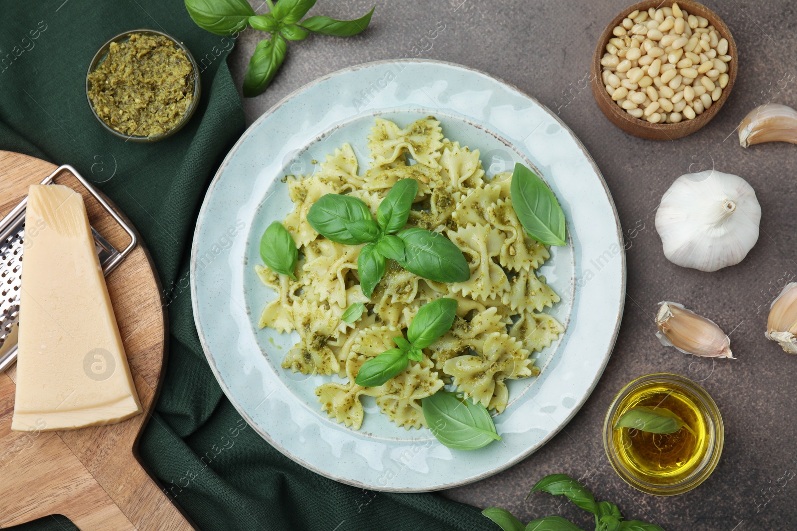 Photo of Delicious pasta with pesto sauce and ingredients on dark textured table, flat lay