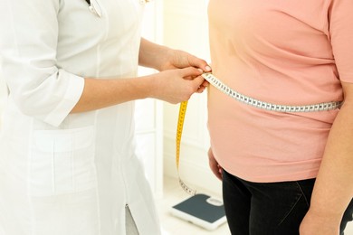 Image of Nutritionist measuring overweight woman's waist with tape in clinic, closeup