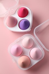 Photo of Makeup sponges in plastic containers on pink background, top view