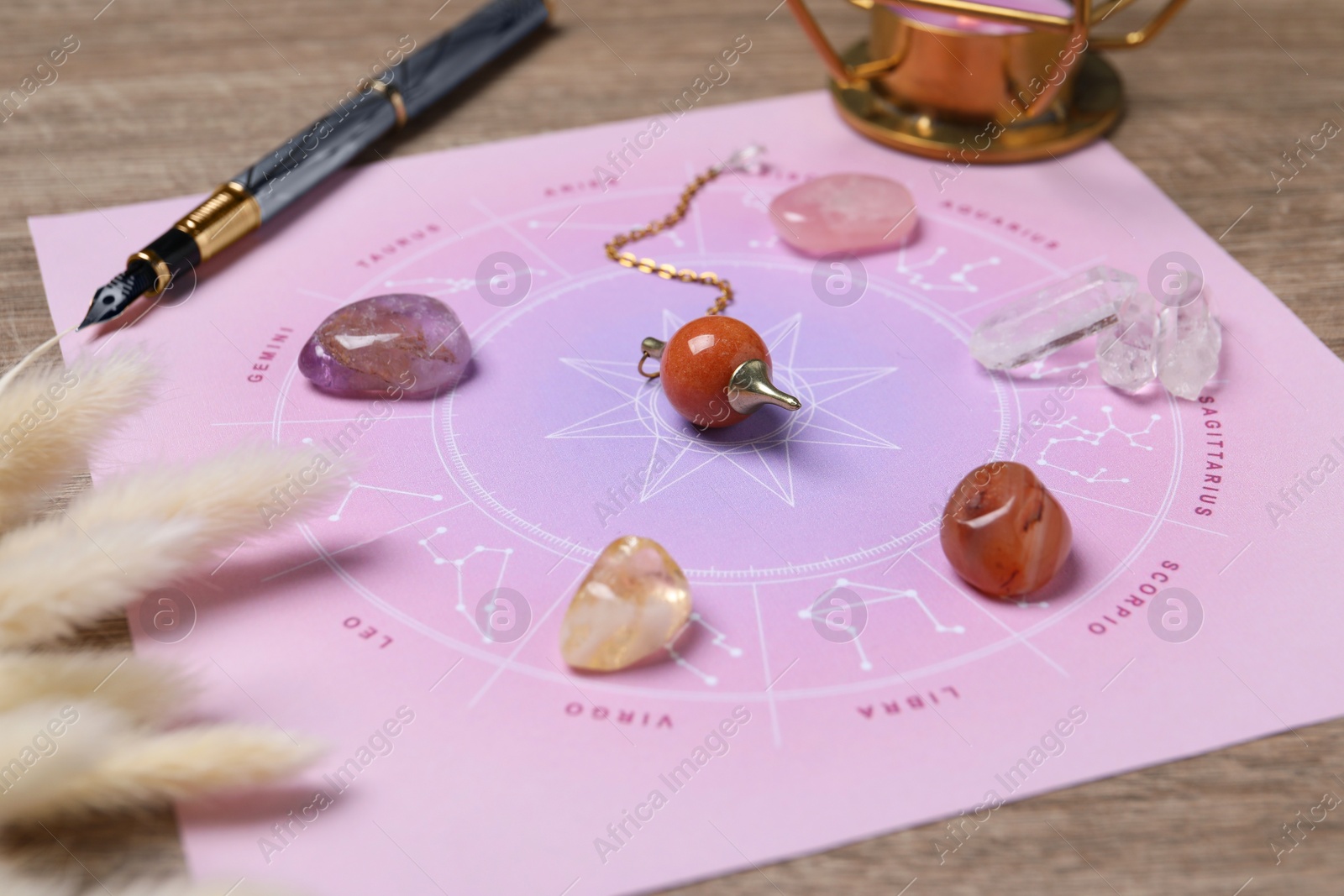 Photo of Astrology prediction. Zodiac wheel, gemstones and pendulum on wooden table, closeup