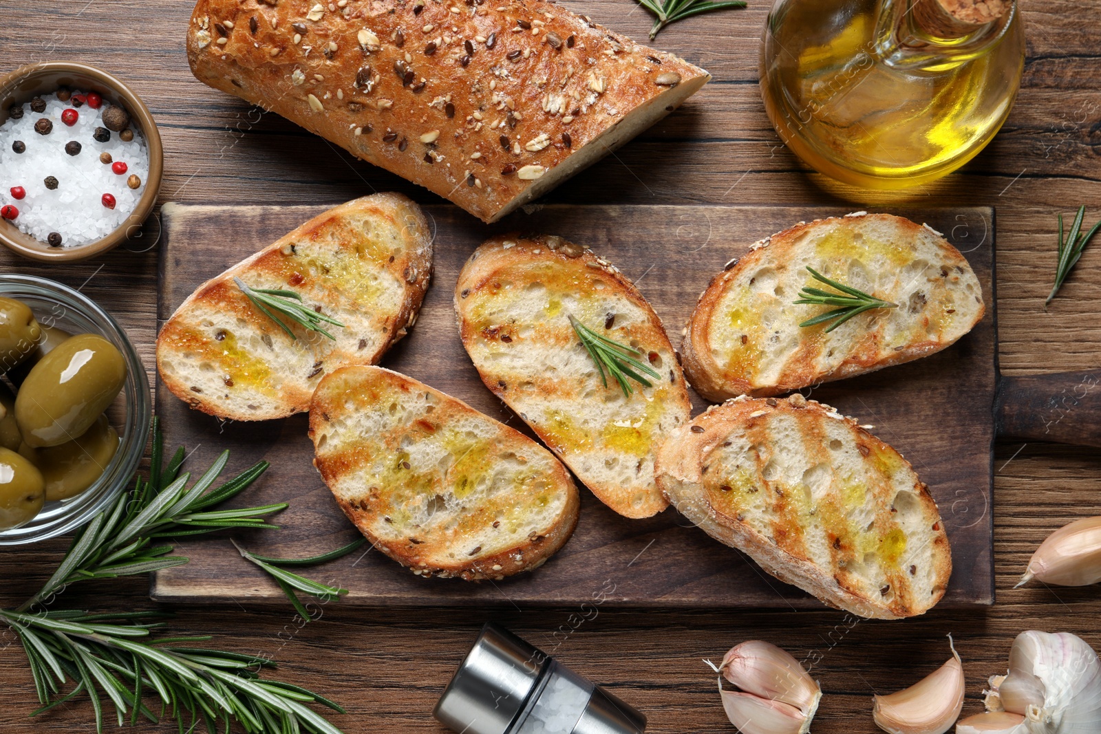 Photo of Tasty bruschettas with oil and rosemary on wooden table, flat lay