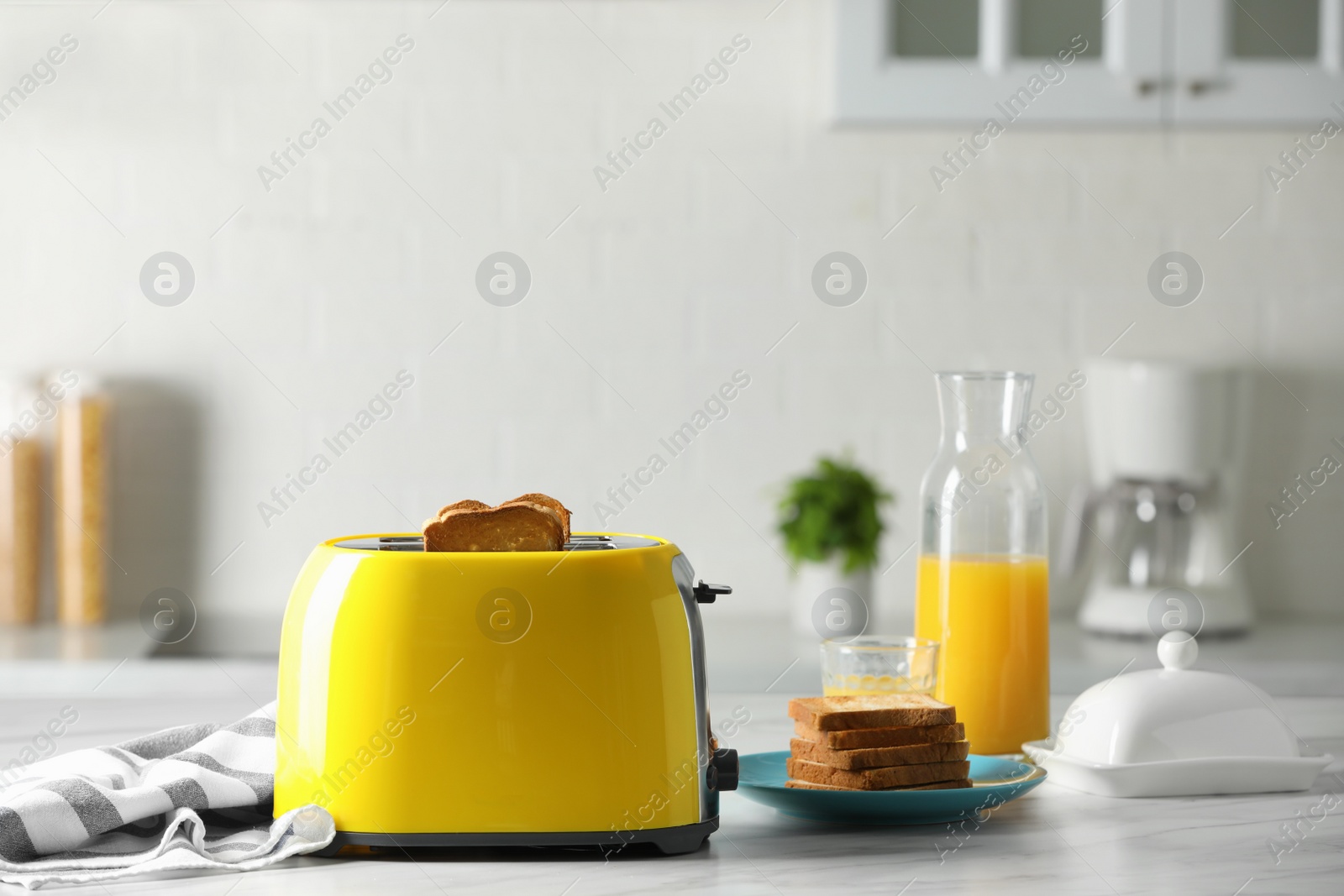 Photo of Yellow toaster with roasted bread slices and orange juice on white marble table