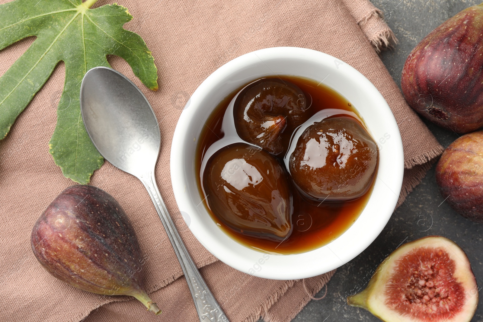 Photo of Bowl of tasty sweet jam, fresh figs and spoon on grey table, flat lay