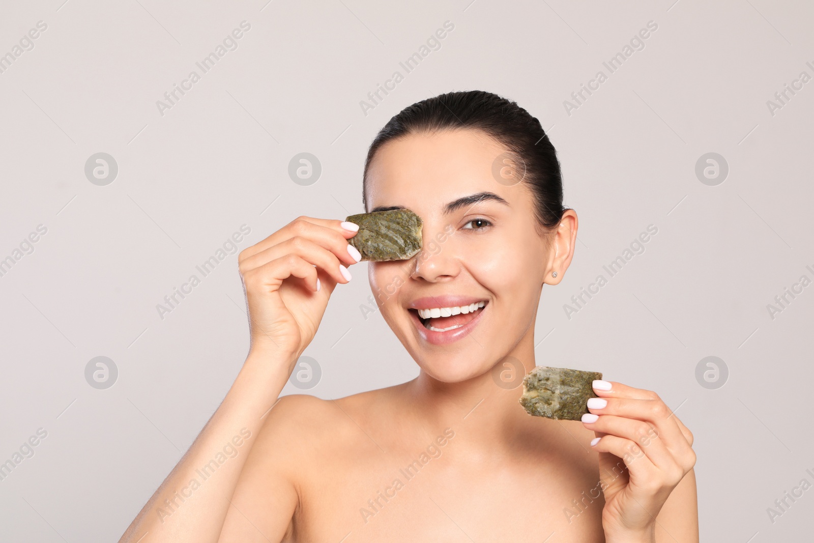 Photo of Beautiful young woman putting green tea bags on eyes against light grey background