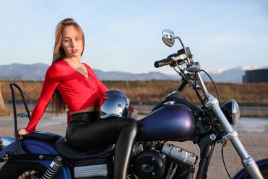 Beautiful young woman with helmet sitting on motorcycle outdoors