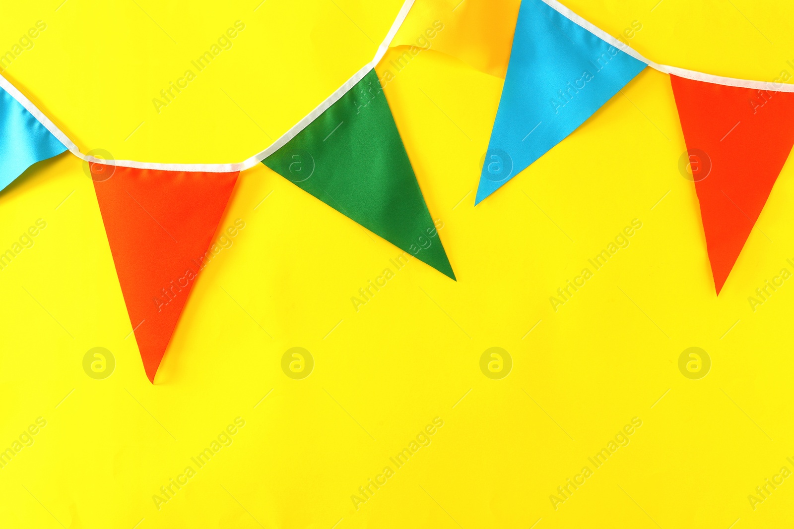 Photo of Bunting with colorful triangular flags on yellow background, space for text