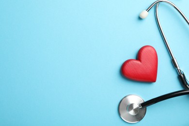 Photo of Stethoscope and red heart on light blue background, top view. Space for text