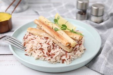 Plate with baked salsify roots, lemon, rice and fork on white wooden table