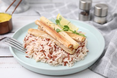 Photo of Plate with baked salsify roots, lemon, rice and fork on white wooden table