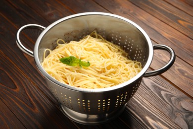 Photo of Cooked pasta in metal colander on wooden table, closeup