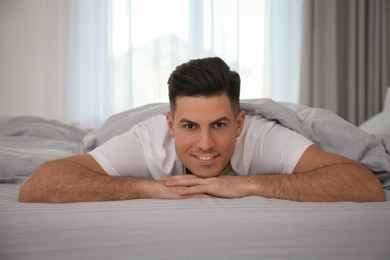 Photo of Man lying in bed with grey linens at home
