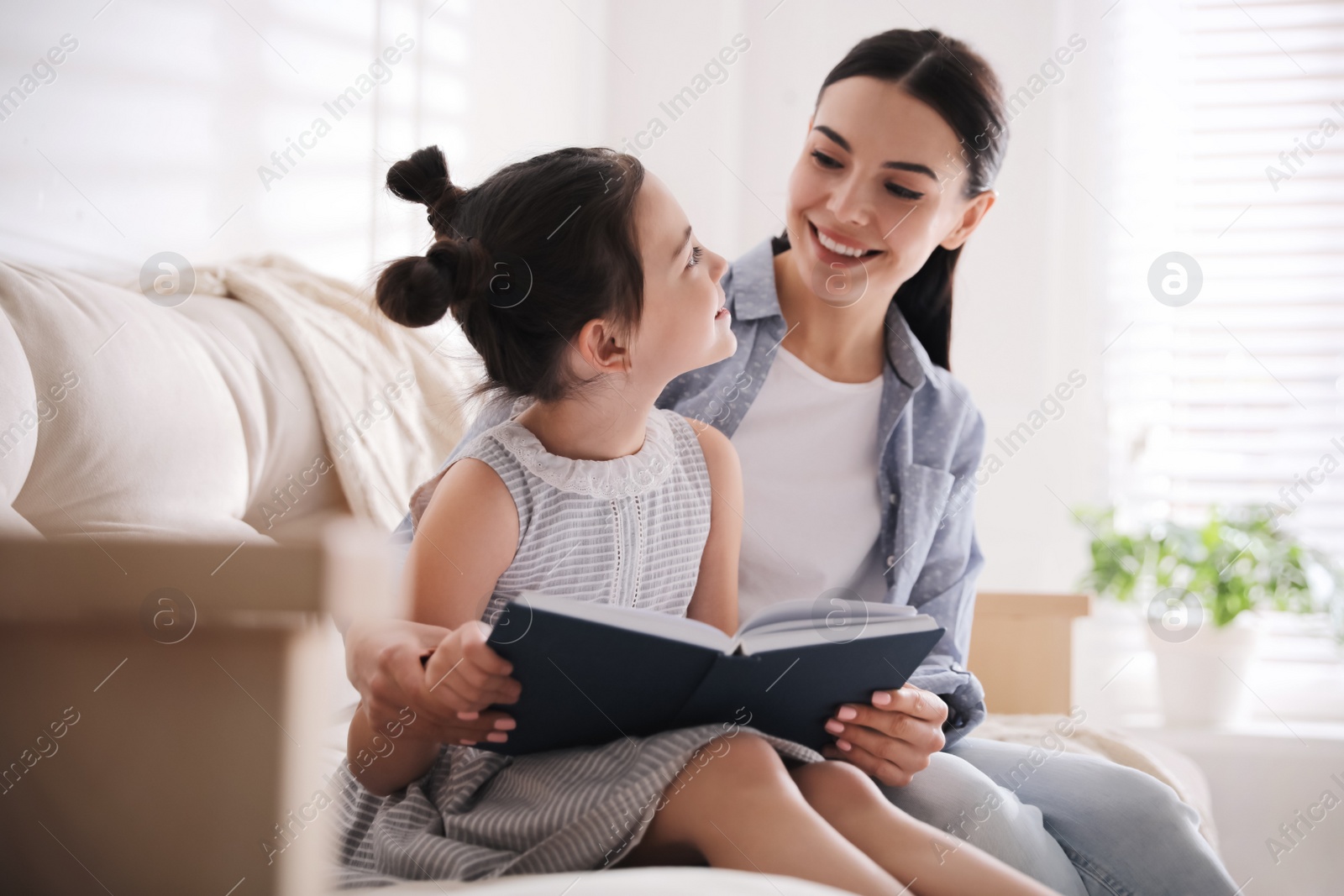 Photo of Little girl with mother reading fairy tale in living room