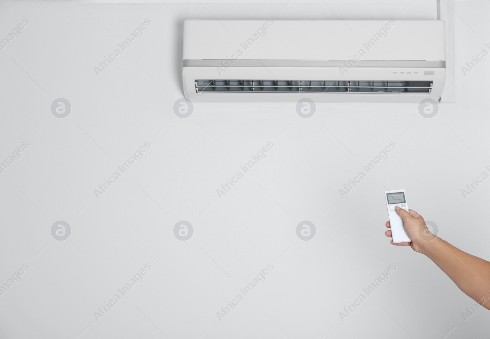 Photo of Man operating air conditioner with remote control indoors, closeup