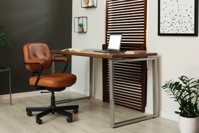 Stylish office interior with comfortable chair, desk and laptop