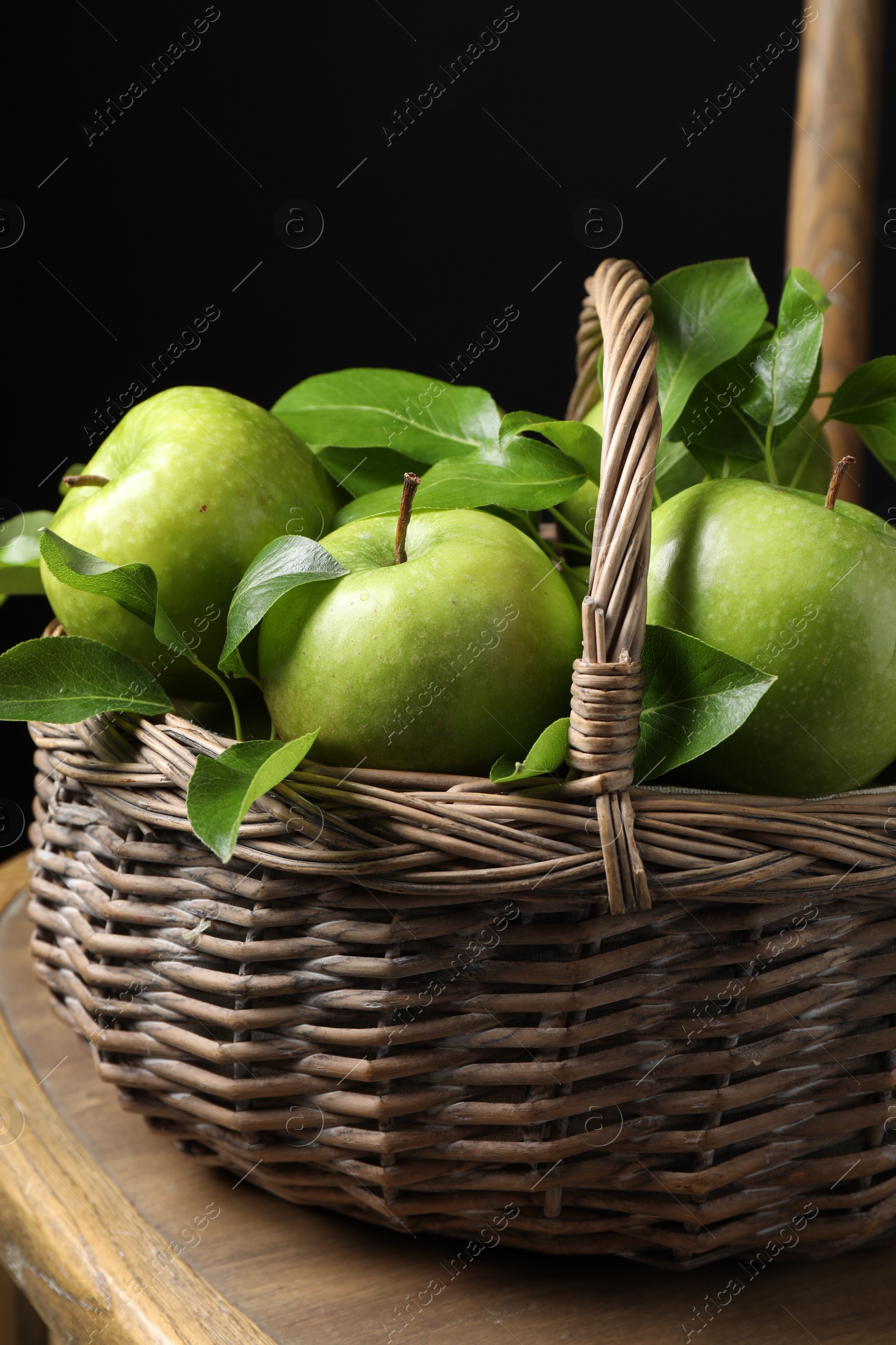 Photo of Fresh ripe green apples and leaves in wicker basket on wooden chair, closeup