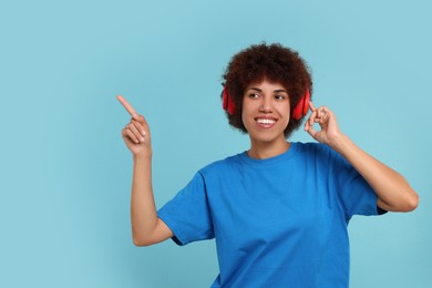 Happy young woman in headphones enjoying music on light blue background. Space for text