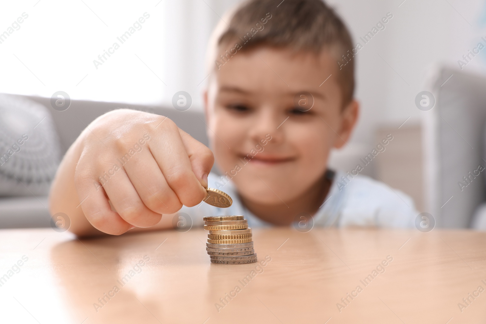 Photo of Cute little boy stacking coins at home, focus on hand