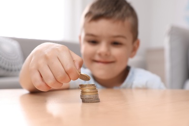 Cute little boy stacking coins at home, focus on hand