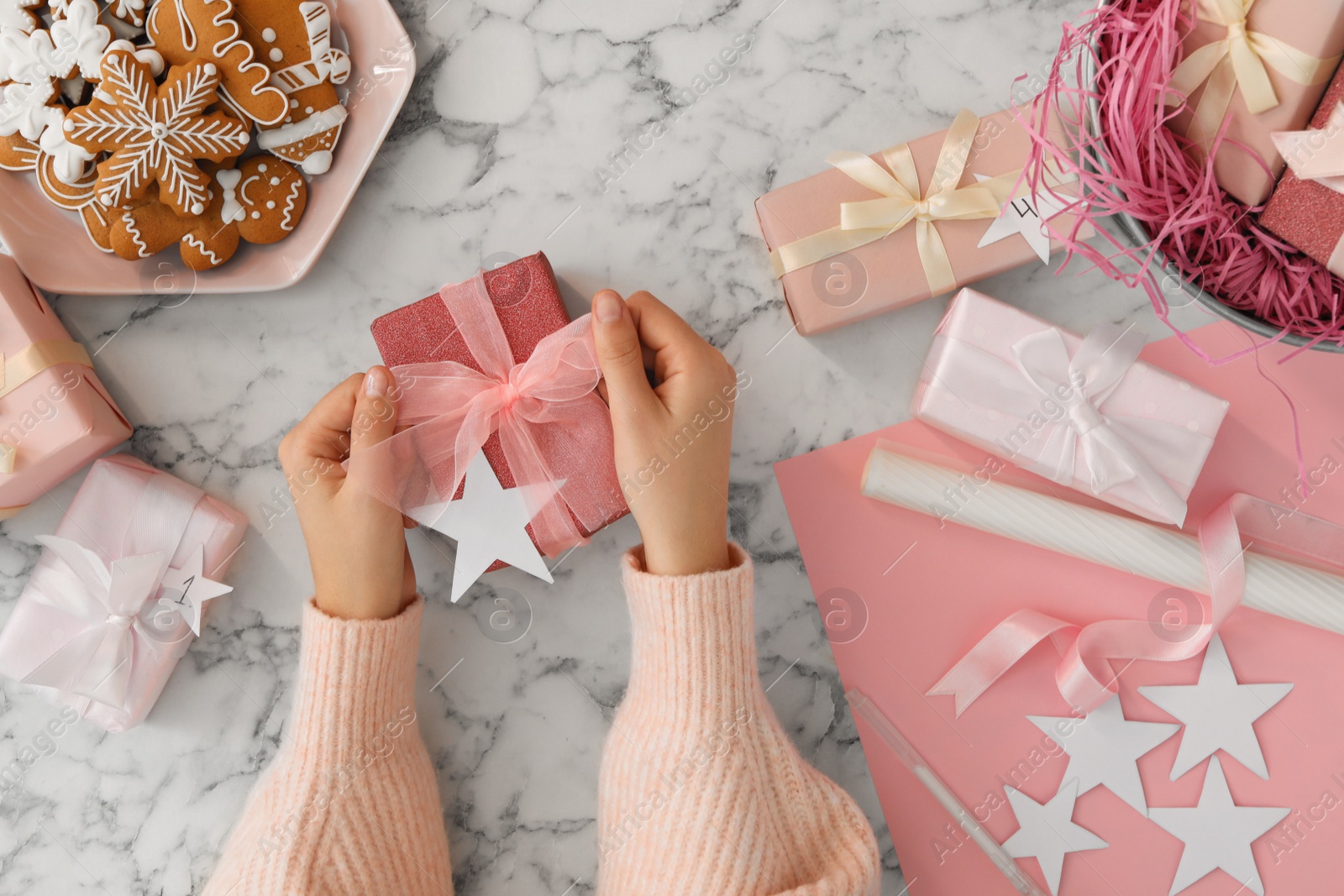 Photo of Woman with gift box at white marble table, top view. Creating advent calendar