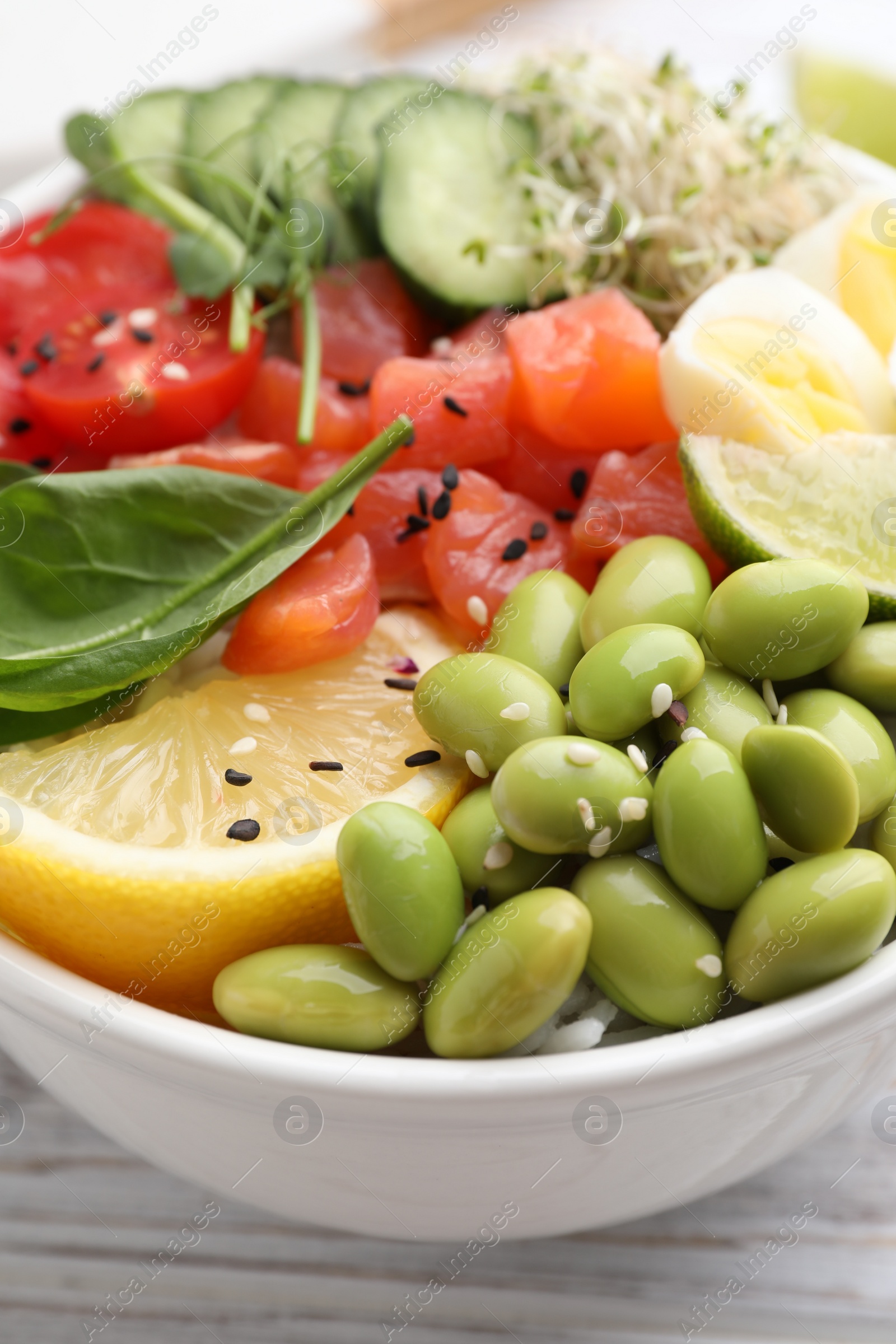 Photo of Delicious poke bowl with quail eggs, fish and edamame beans on white wooden table, closeup