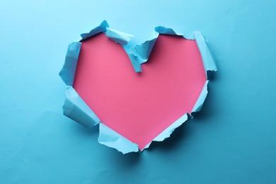 Torn heart shaped hole in light blue paper on pink background