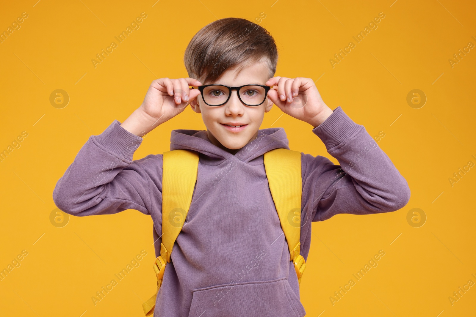 Photo of Cute schoolboy in glasses on orange background