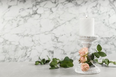 White candlestick with burning candle and floral decor on light stone table. Space for text
